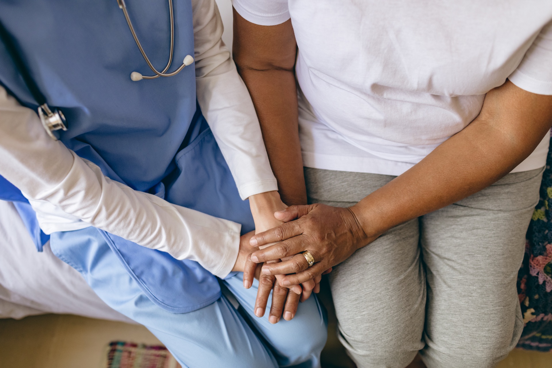A healthcare worker holding an older patient's hands during a consultation