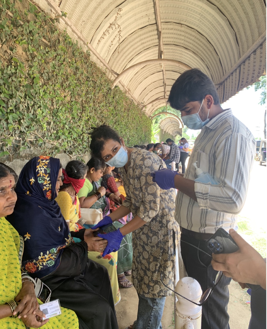 Tricog volunteers screening seated patients along a shaded corridor at the Village Clinic