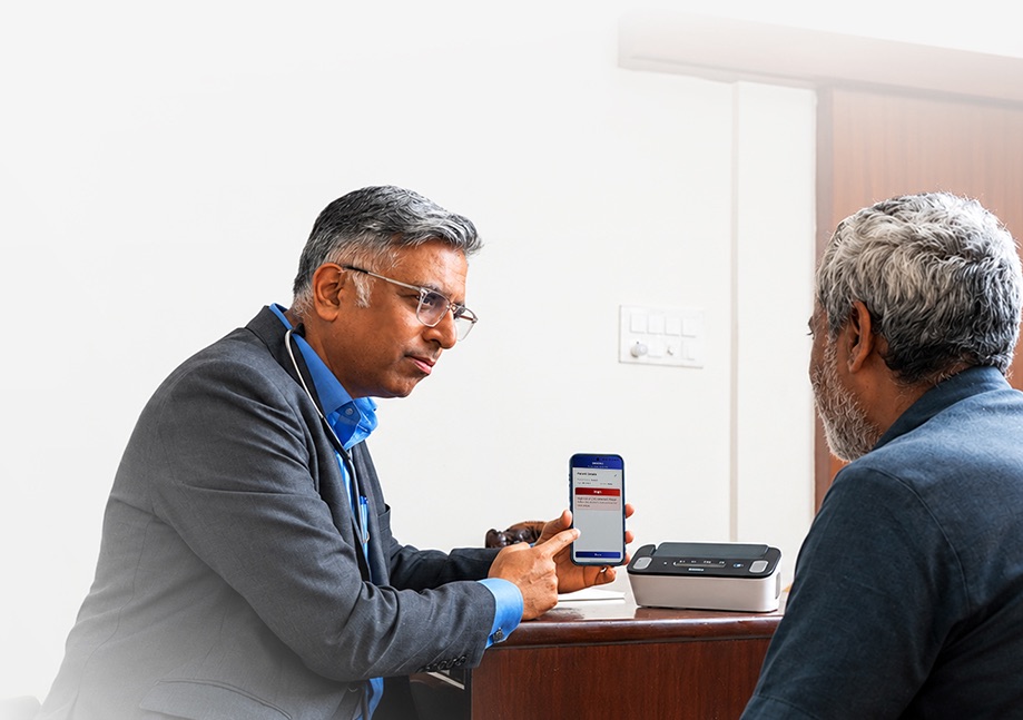 A doctor and a patient in consultation, reviewing a single-lead ECG on a Tricog CardioCheck device.